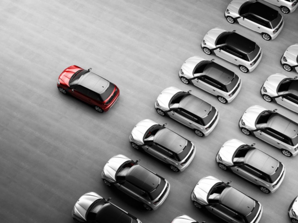 A fleet of grey cars with one red one in front of them