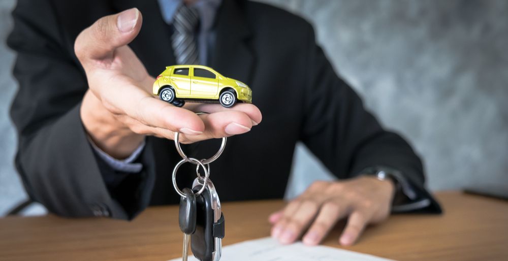 A leasing exec hands over car keys with a toy of a yellow hatchback on them